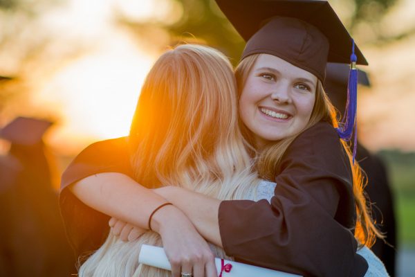 Two high school graduates are hugging after the graduation ceremony.